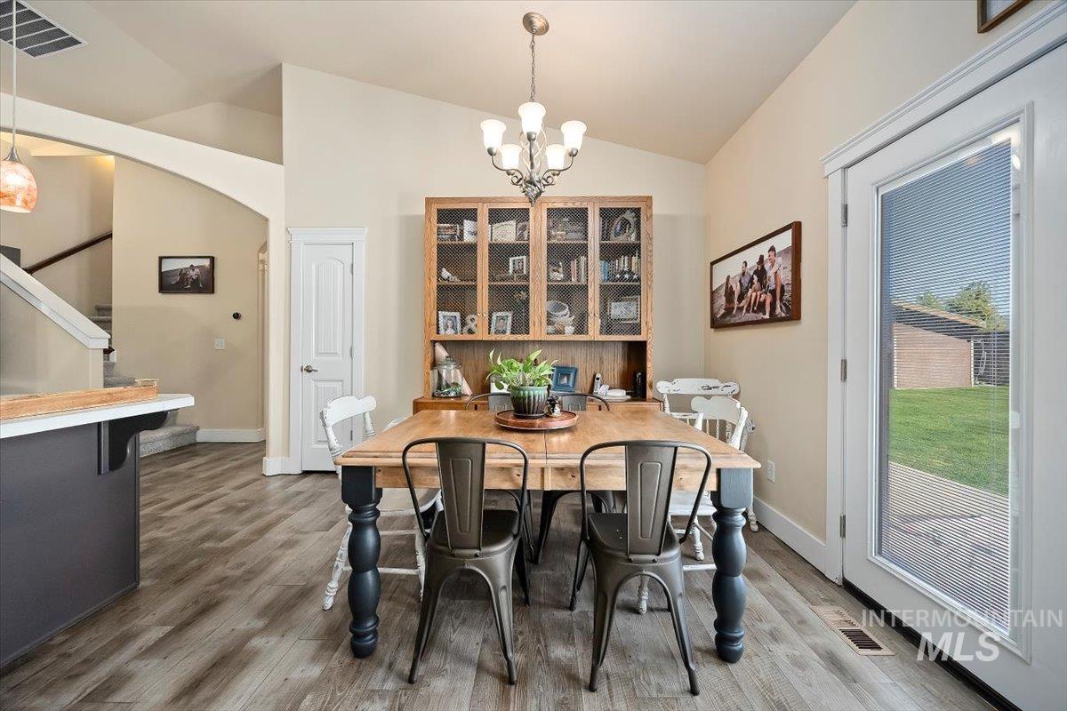 Dining space with a chandelier, lofted ceiling, light wood-style floors, arched walkways, and stairway