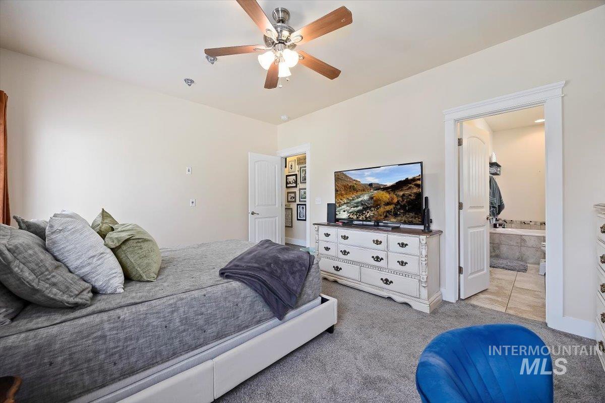 Bedroom featuring light carpet, light tile patterned floors, a ceiling fan, and connected bathroom
