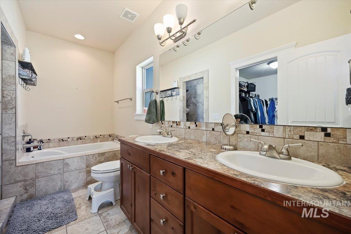 Bathroom featuring a bath, a walk in closet, double vanity, light tile patterned flooring, and tasteful backsplash