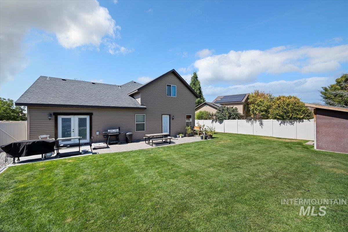 Back of property with a fenced backyard, a patio area, a shingled roof, and french doors