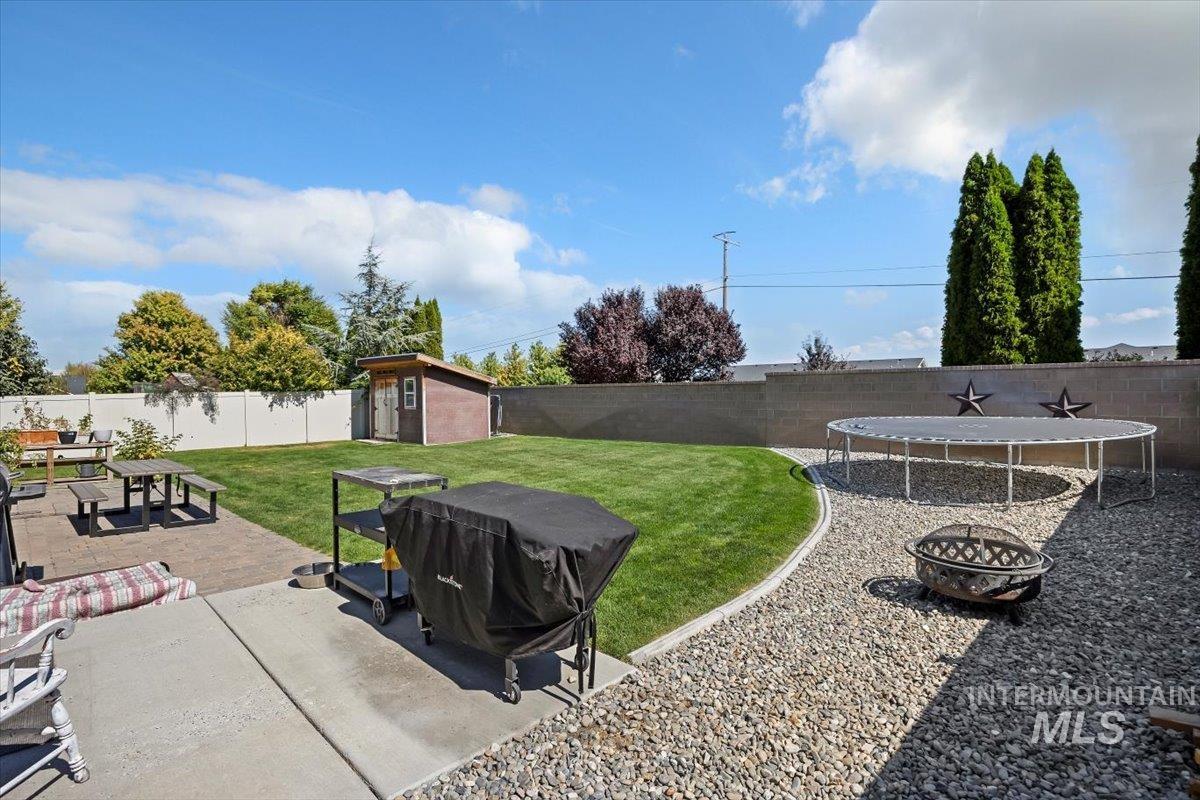 Fenced backyard featuring an outdoor fire pit, a patio area, a trampoline, and a shed