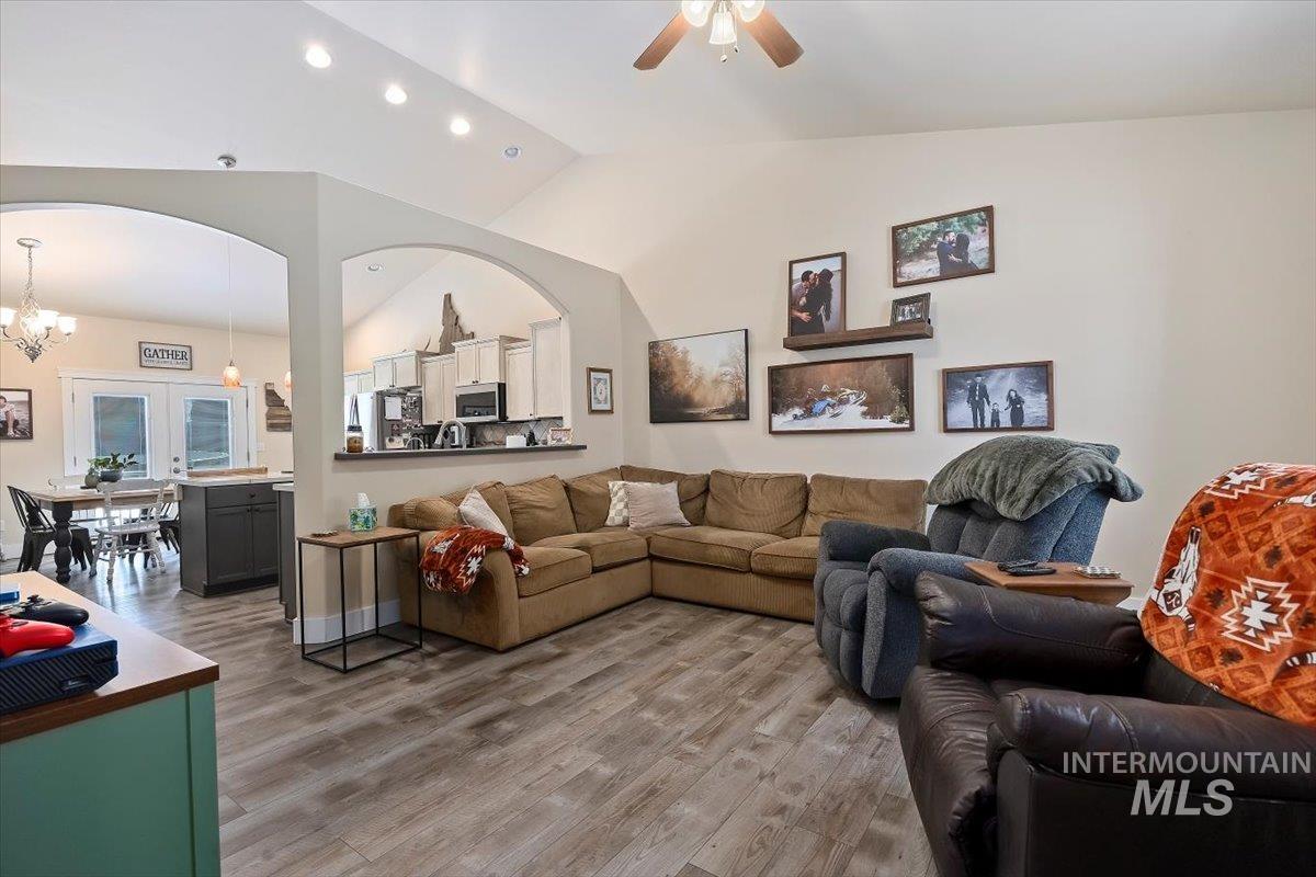 Living room featuring lofted ceiling, wood finished floors, ceiling fan, a chandelier, and recessed lighting