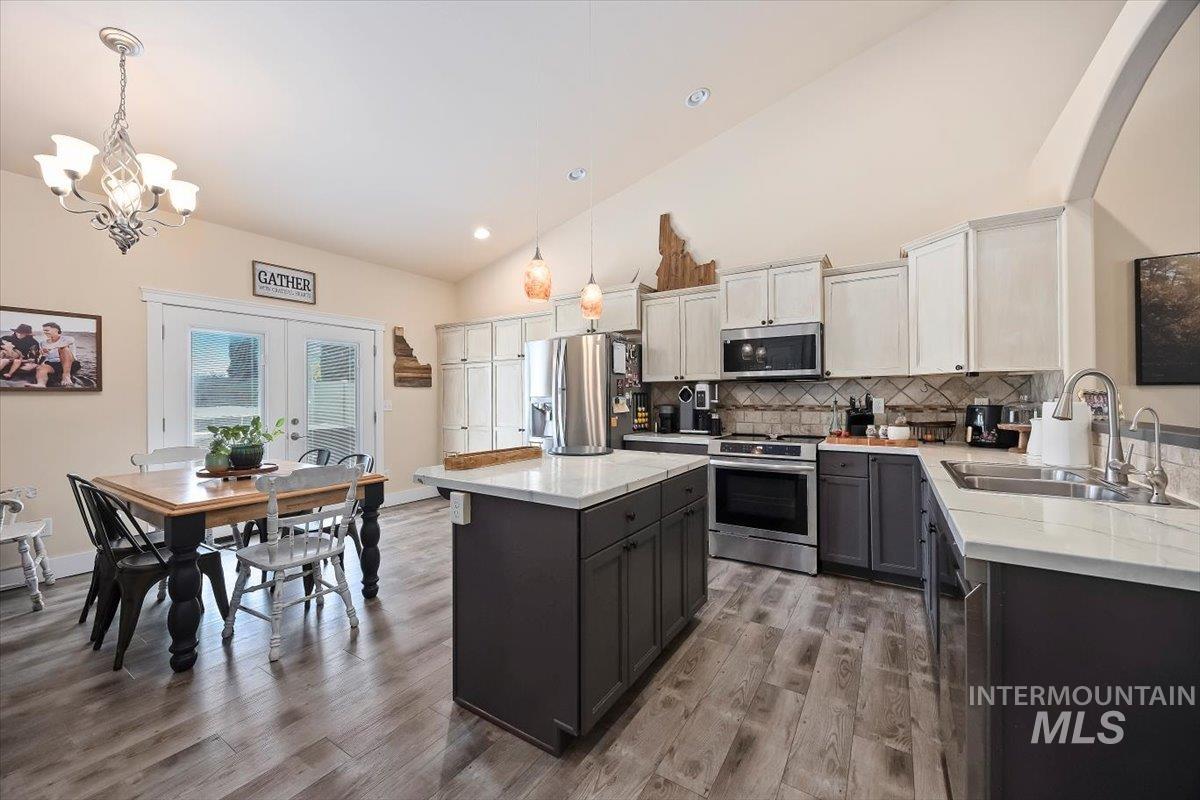 Kitchen featuring tasteful backsplash, stainless steel appliances, white cabinets, light wood-type flooring, and high vaulted ceiling