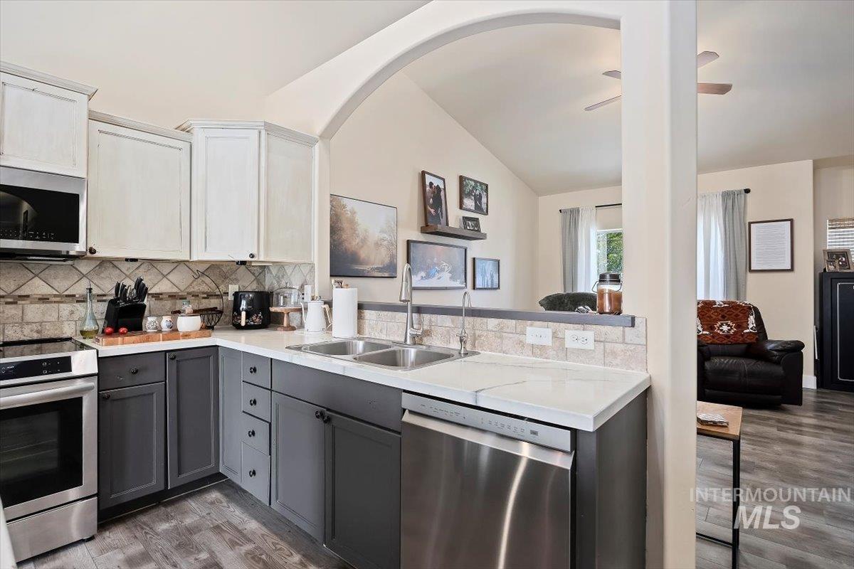 Kitchen with gray cabinetry, appliances with stainless steel finishes, white cabinets, backsplash, and light wood-style flooring