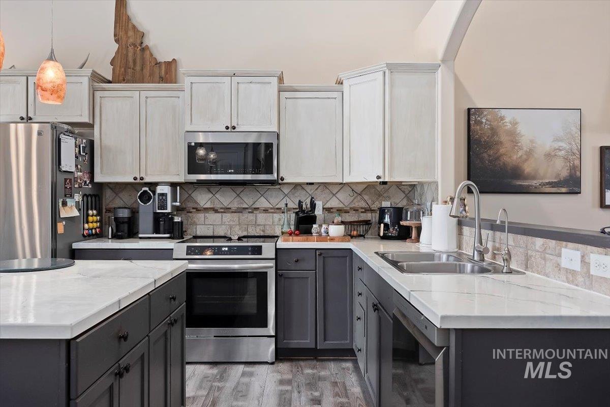Kitchen with gray cabinetry, appliances with stainless steel finishes, tasteful backsplash, and decorative light fixtures
