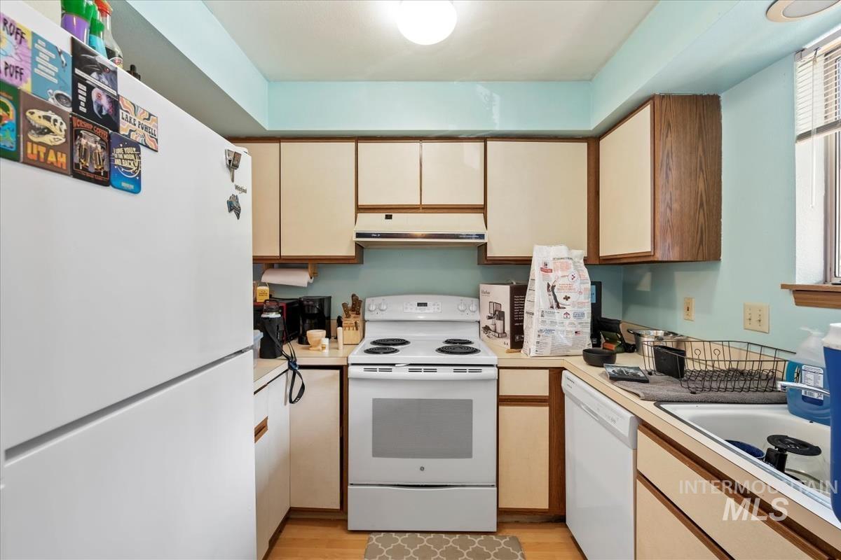 Kitchen featuring white appliances, light countertops, under cabinet range hood, light wood finished floors, and brown cabinets