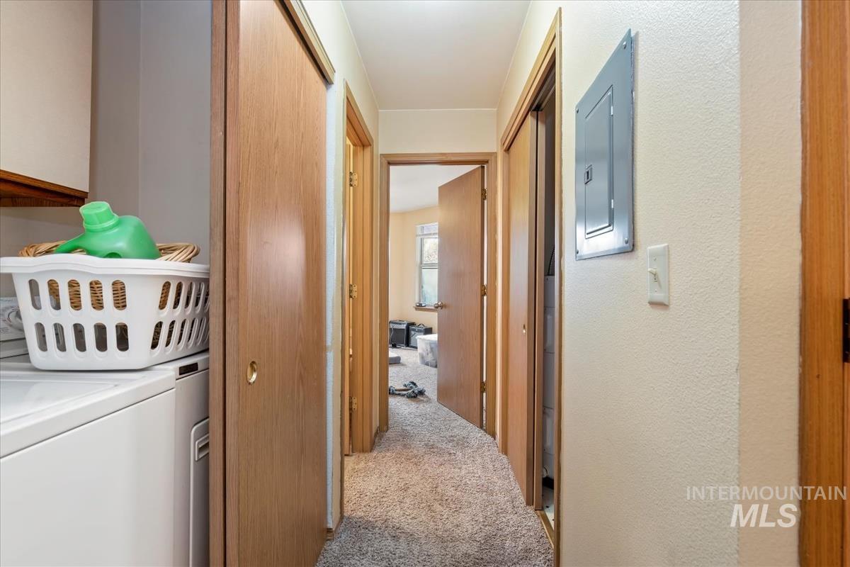 Hallway with light carpet, electric panel, and separate washer and dryer