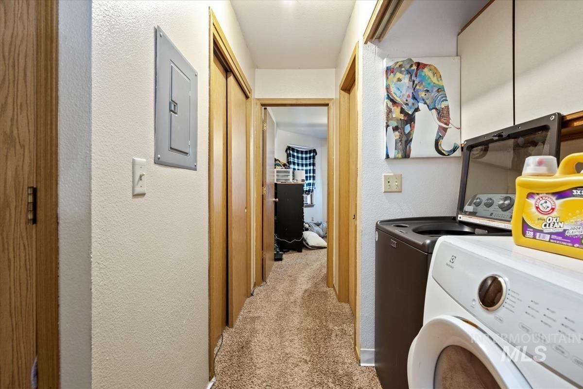 Laundry room with a textured wall, light carpet, electric panel, and independent washer and dryer