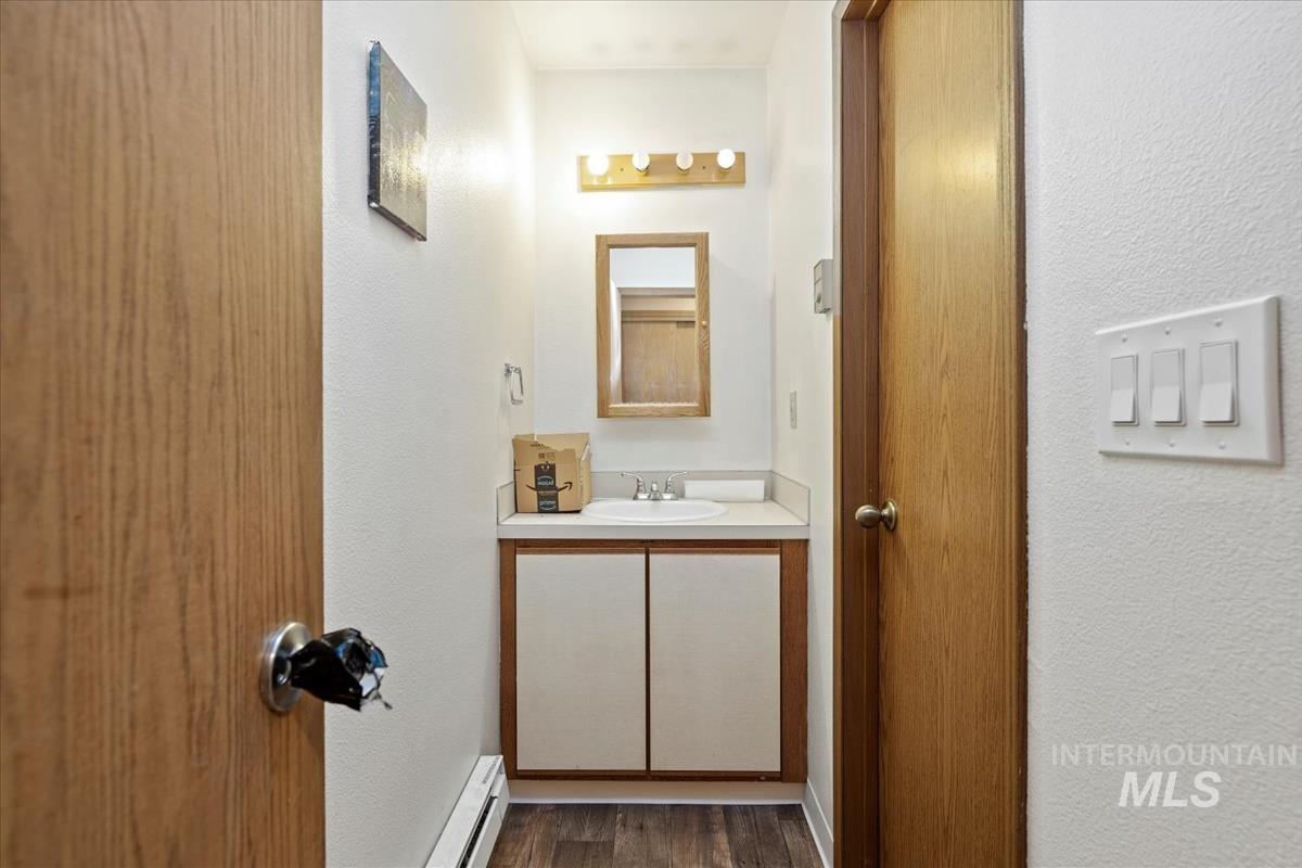 Bathroom featuring a textured wall, vanity, a baseboard radiator, and dark wood-style floors