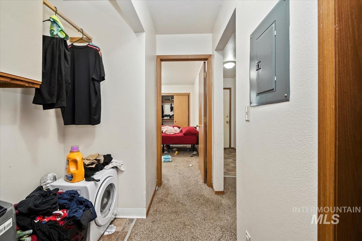 Hallway with electric panel, light colored carpet, and washer / clothes dryer