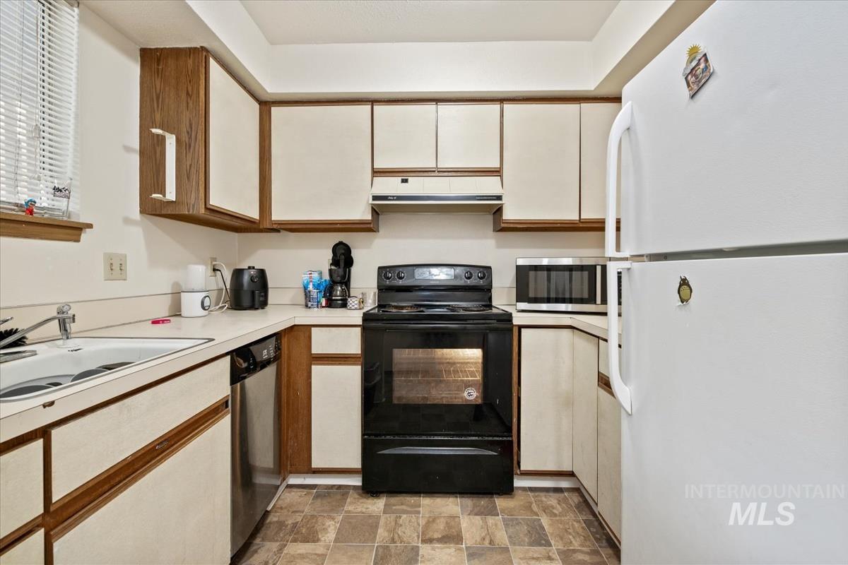 Kitchen featuring appliances with stainless steel finishes, light countertops, stone finish flooring, and brown cabinetry