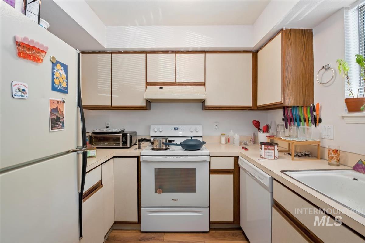 Kitchen featuring white appliances, light countertops, brown cabinets, and white cabinetry