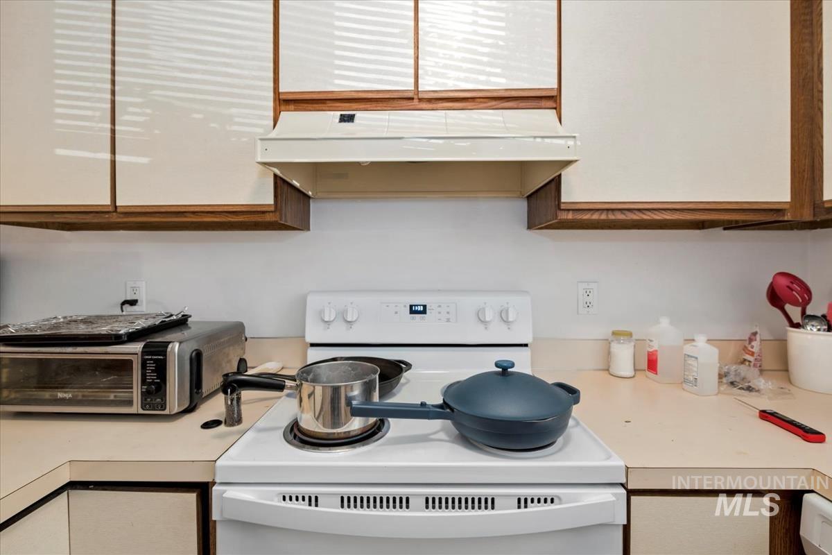Kitchen featuring electric stove, light countertops, and under cabinet range hood