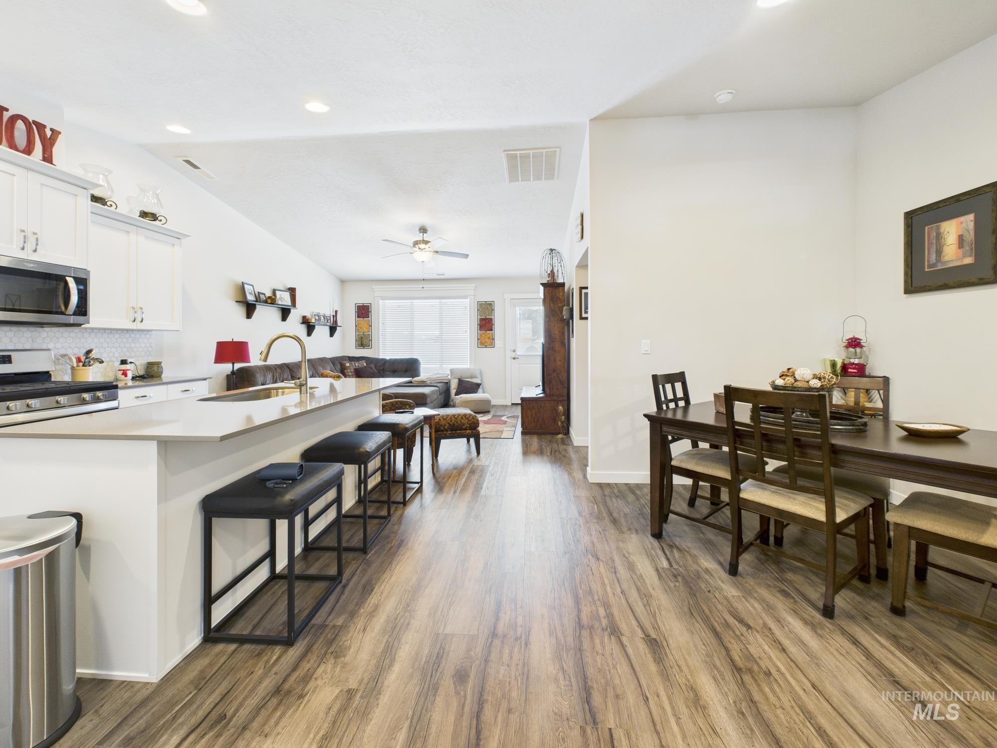 Kitchen featuring white cabinetry, dark wood-style flooring, appliances with stainless steel finishes, a kitchen bar, and open floor plan