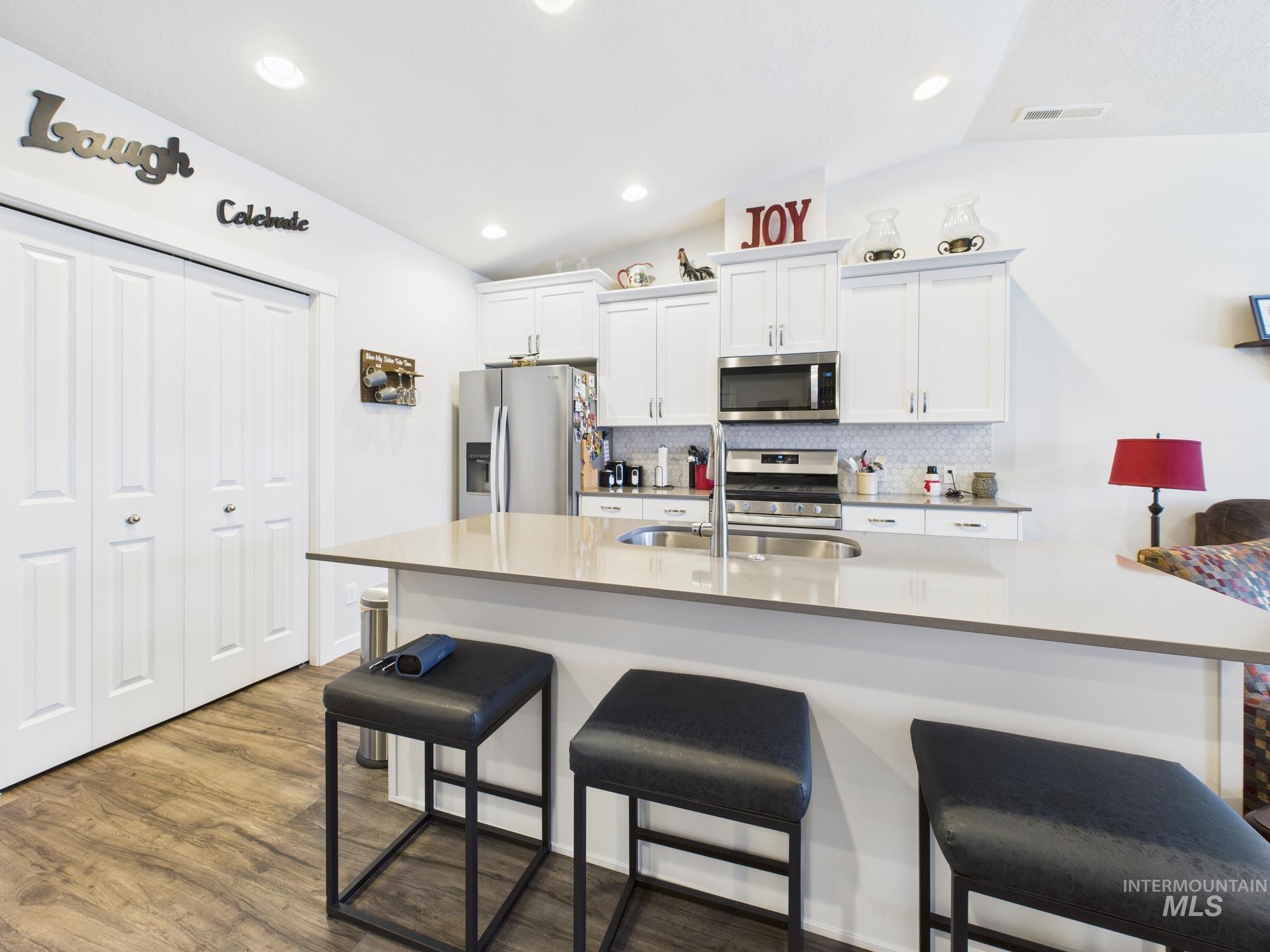 Kitchen with a breakfast bar, tasteful backsplash, appliances with stainless steel finishes, white cabinetry, and dark wood finished floors