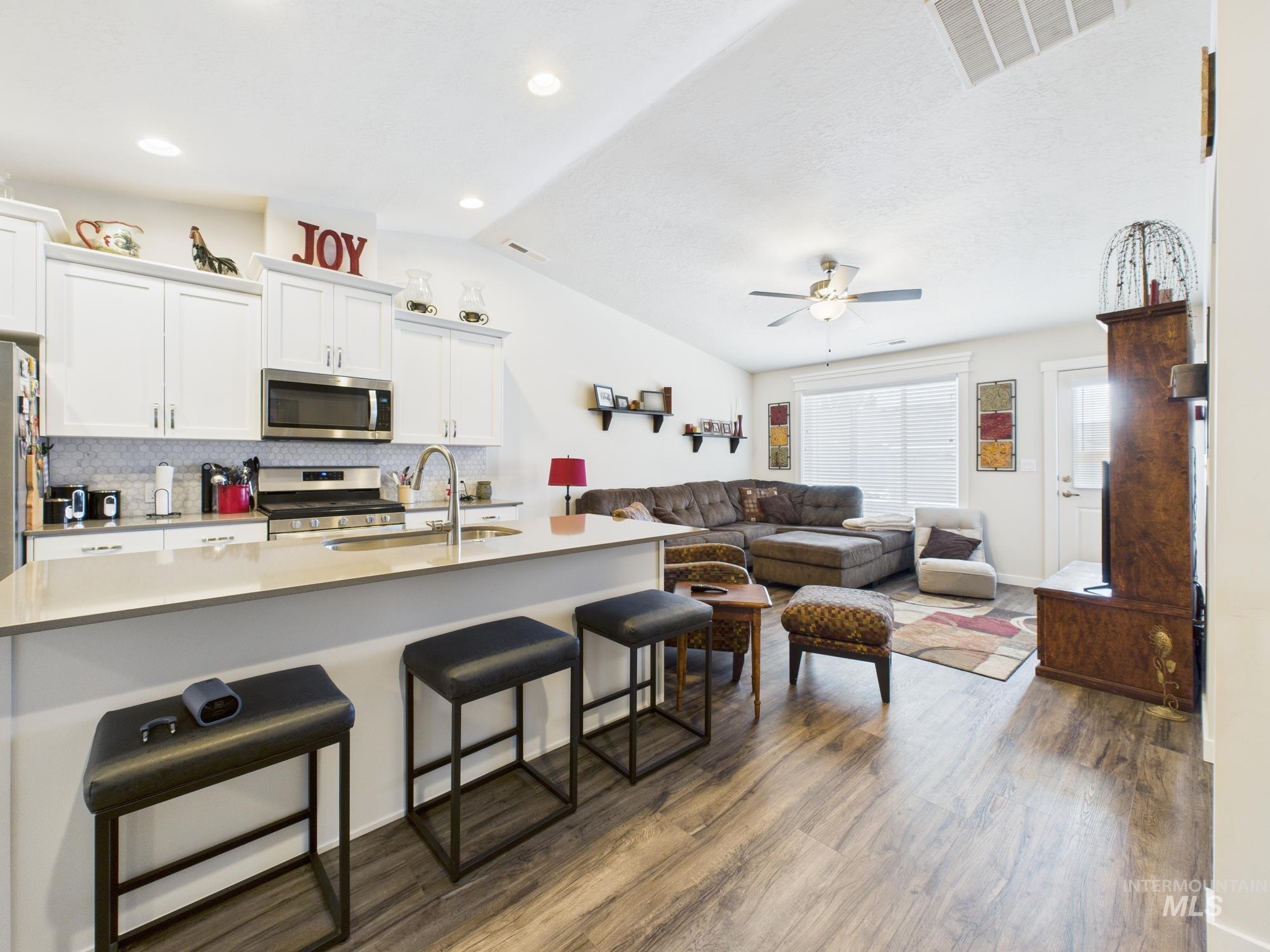Kitchen with white cabinets, a kitchen breakfast bar, stainless steel appliances, backsplash, and a center island with sink