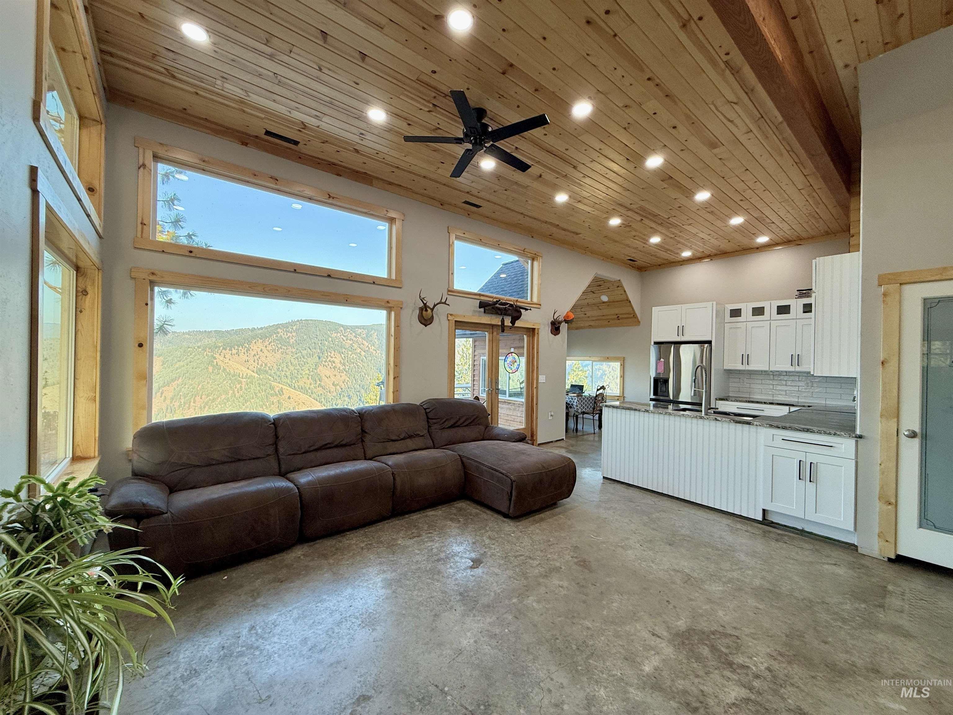 Living room with wood ceiling, finished concrete flooring, ceiling fan, a high ceiling, and recessed lighting