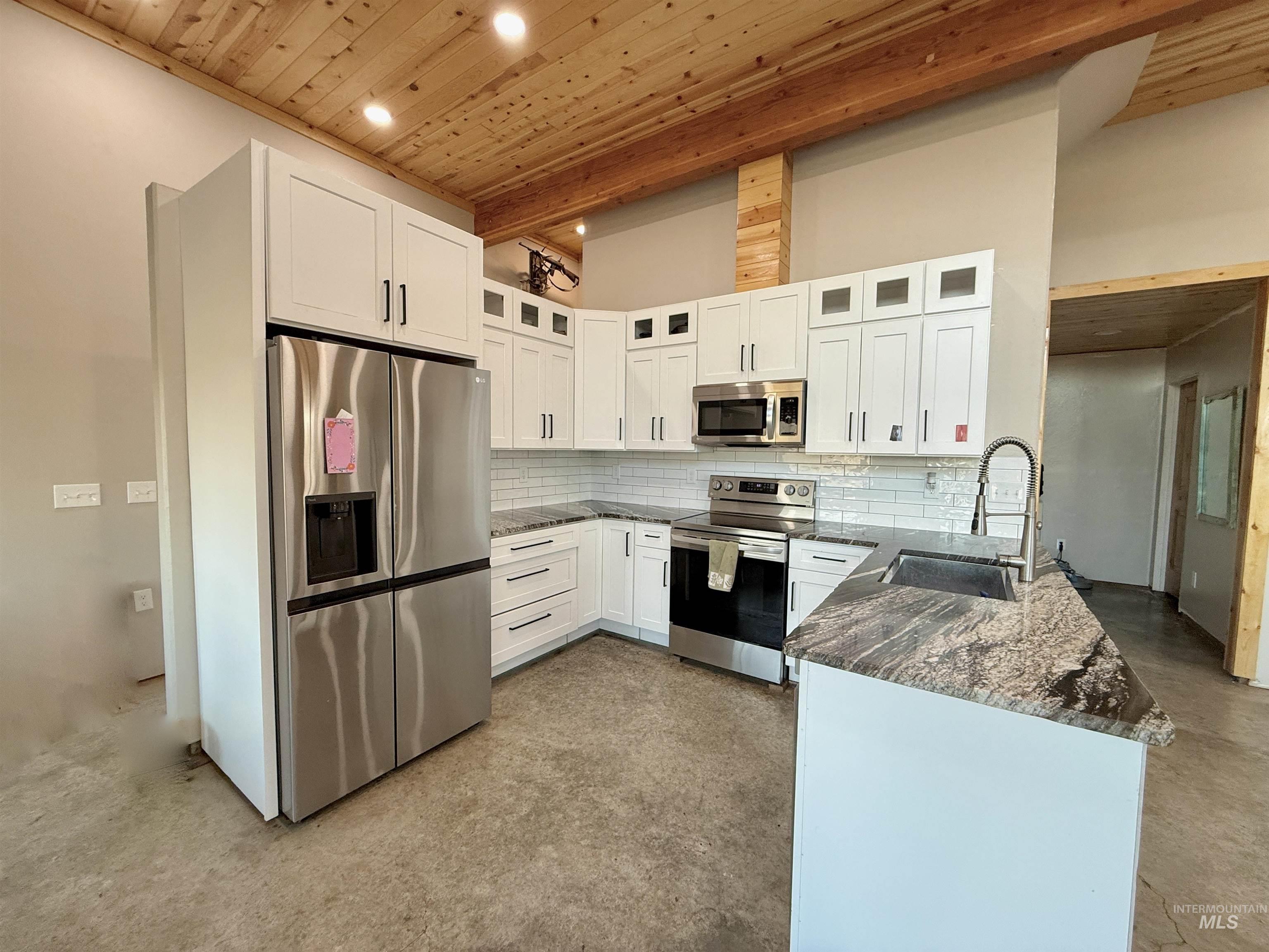 Kitchen featuring stainless steel appliances, tasteful backsplash, a peninsula, a wood ceiling with exposed beams, and white cabinetry