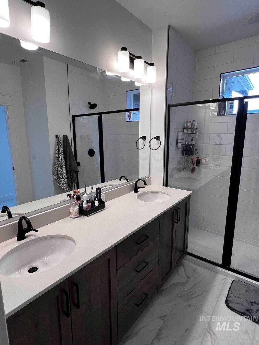 Bathroom with double vanity, a stall shower, and light marble finish floors