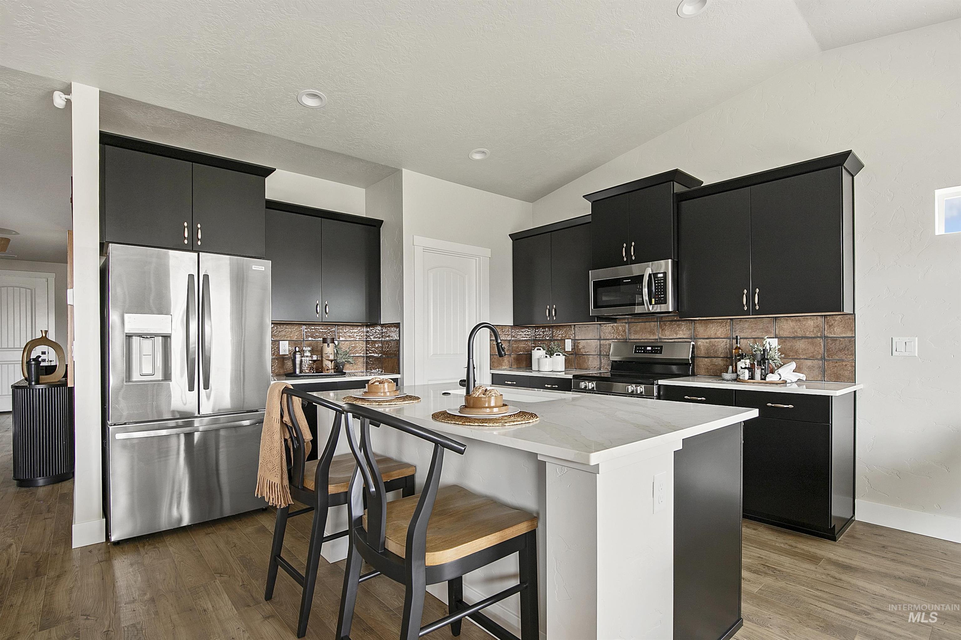 Kitchen with dark cabinets, stainless steel appliances, a breakfast bar, a center island with sink, and recessed lighting