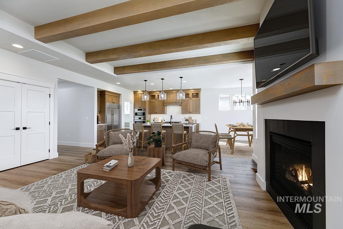 Living room with light wood-style flooring, recessed lighting, beam ceiling, a glass covered fireplace, and a chandelier