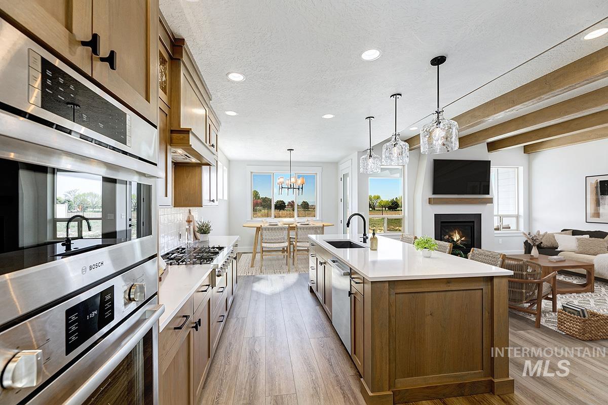Kitchen with stainless steel appliances, brown cabinetry, light wood-style flooring, a warm lit fireplace, and recessed lighting