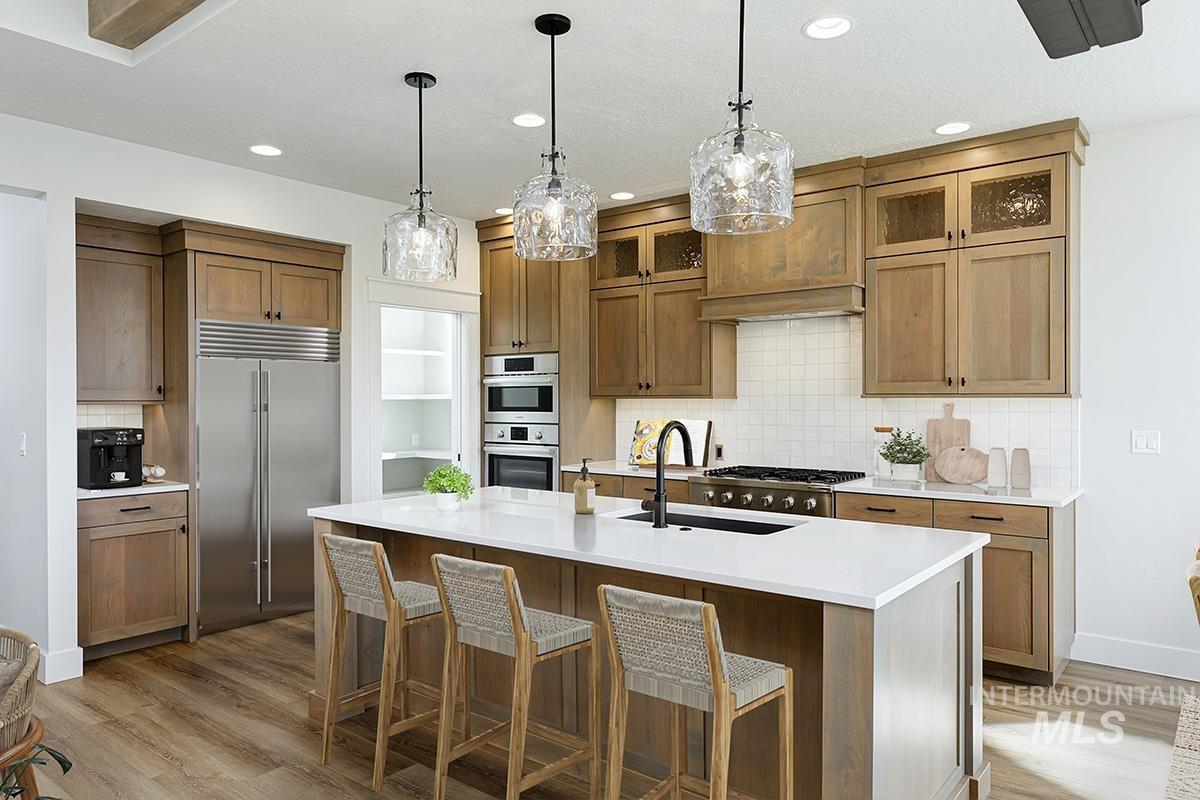 Kitchen with tasteful backsplash, stainless steel appliances, hanging light fixtures, a breakfast bar area, and brown cabinetry