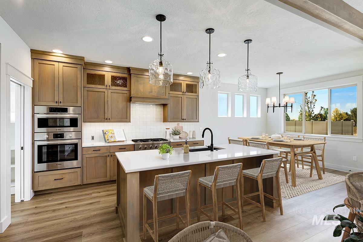 Kitchen with hanging light fixtures, decorative backsplash, light wood-style flooring, brown cabinets, and a kitchen island with sink