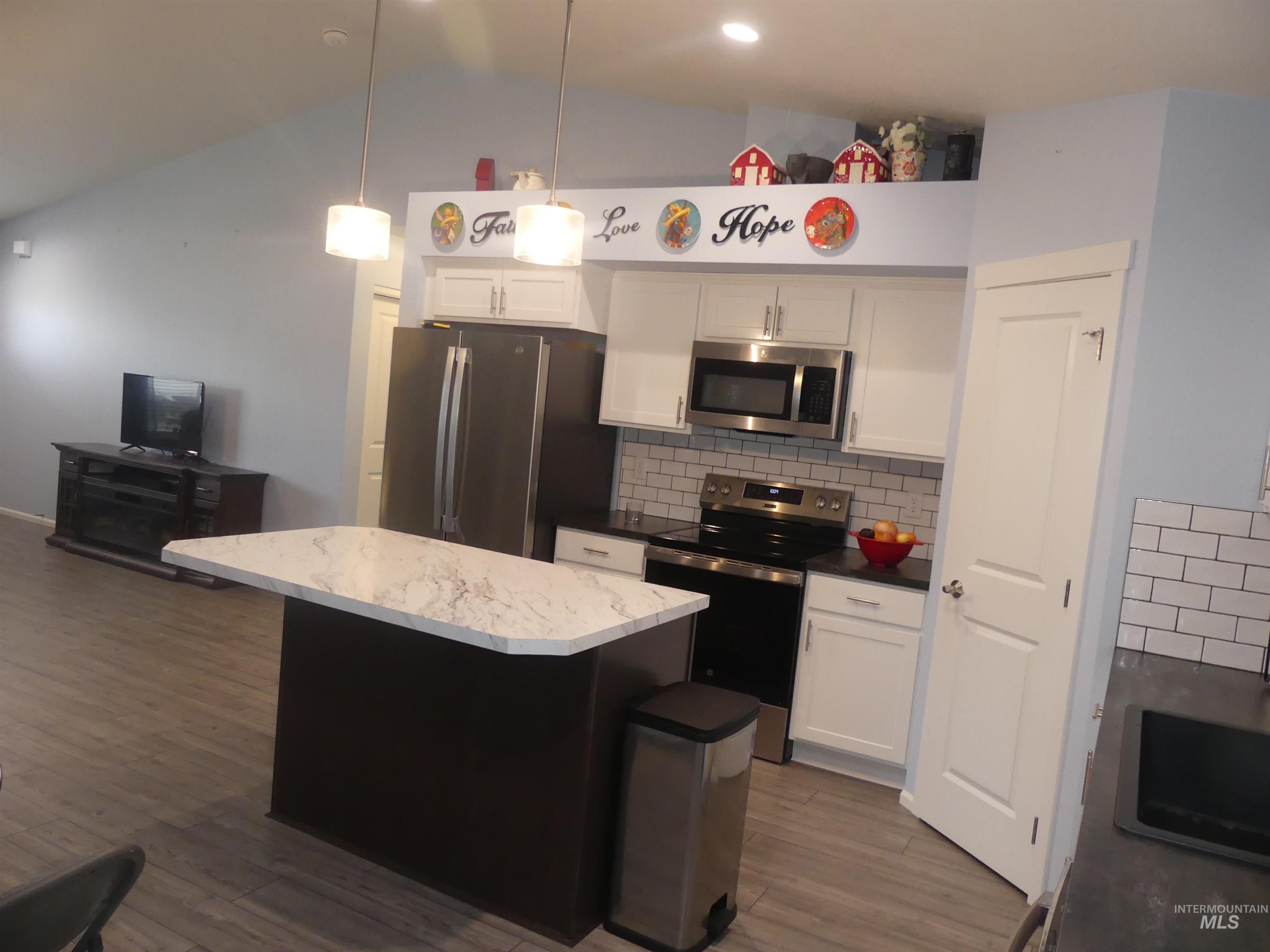 Kitchen with backsplash, appliances with stainless steel finishes, white cabinets, a center island, and pendant lighting