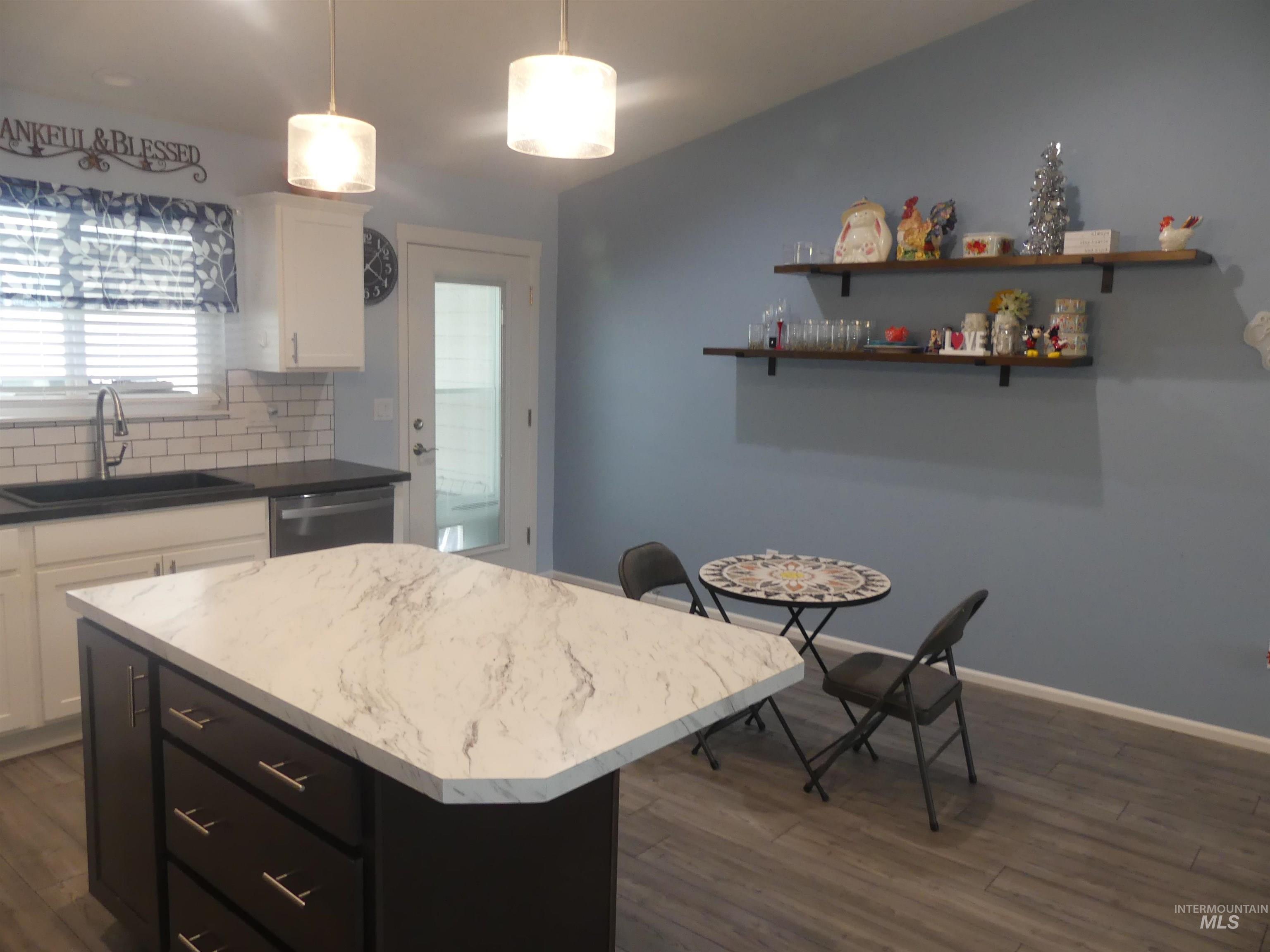 Kitchen featuring white cabinetry, decorative backsplash, hanging light fixtures, a kitchen island, and dark wood finished floors