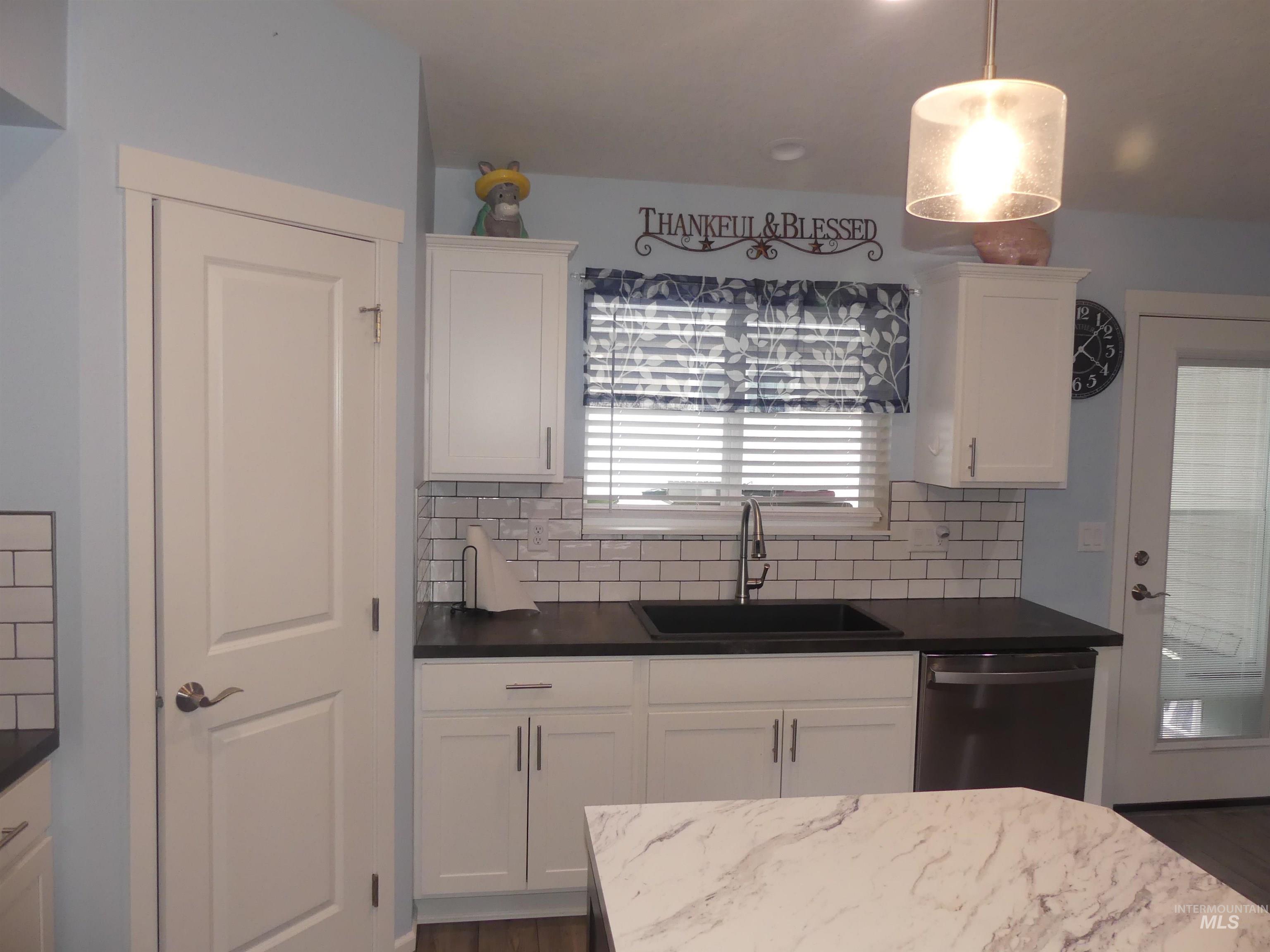 Kitchen with white cabinetry, stainless steel dishwasher, and hanging light fixtures