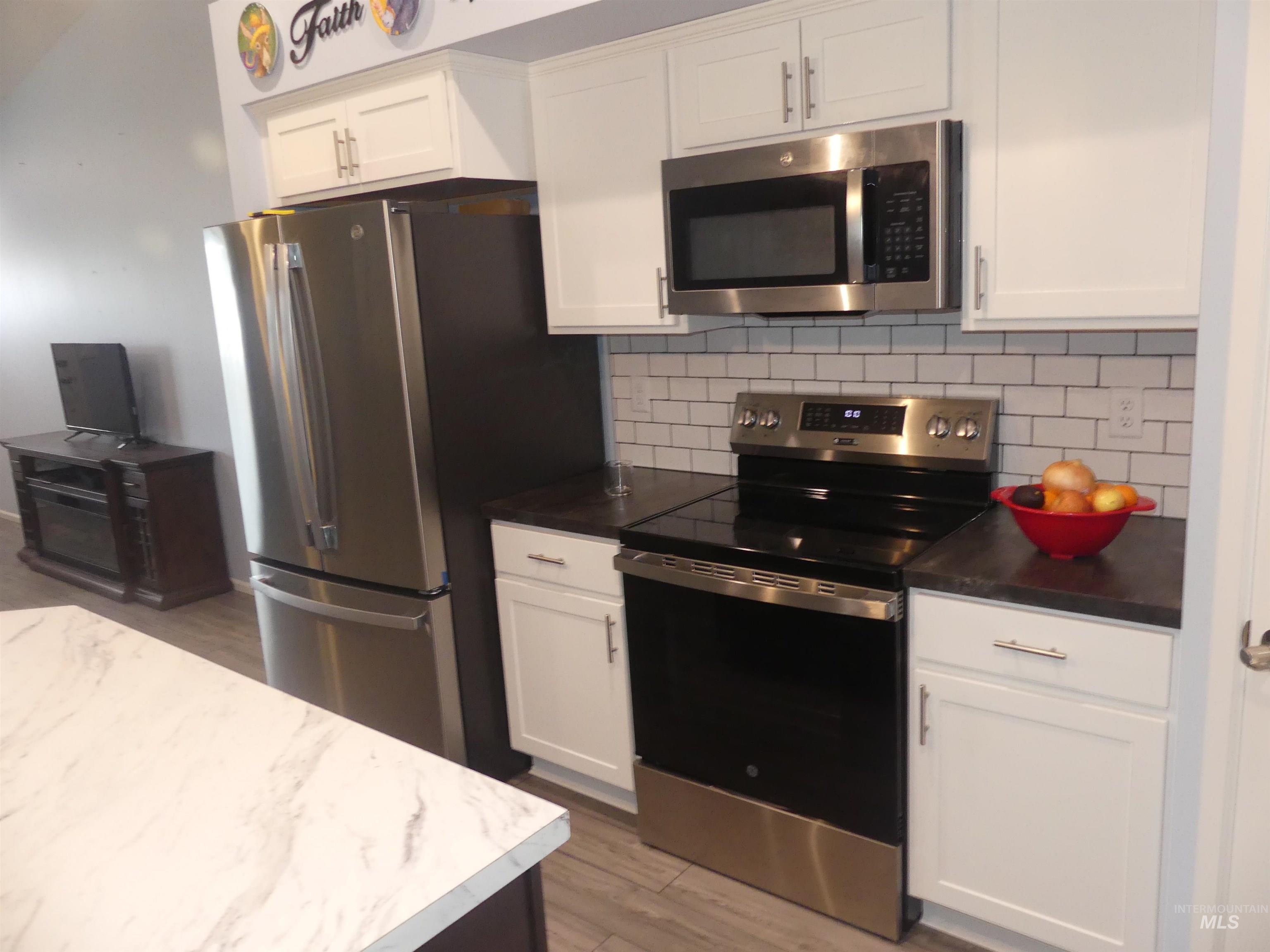 Kitchen with stainless steel appliances, white cabinetry, tasteful backsplash, light wood-type flooring, and dark countertops