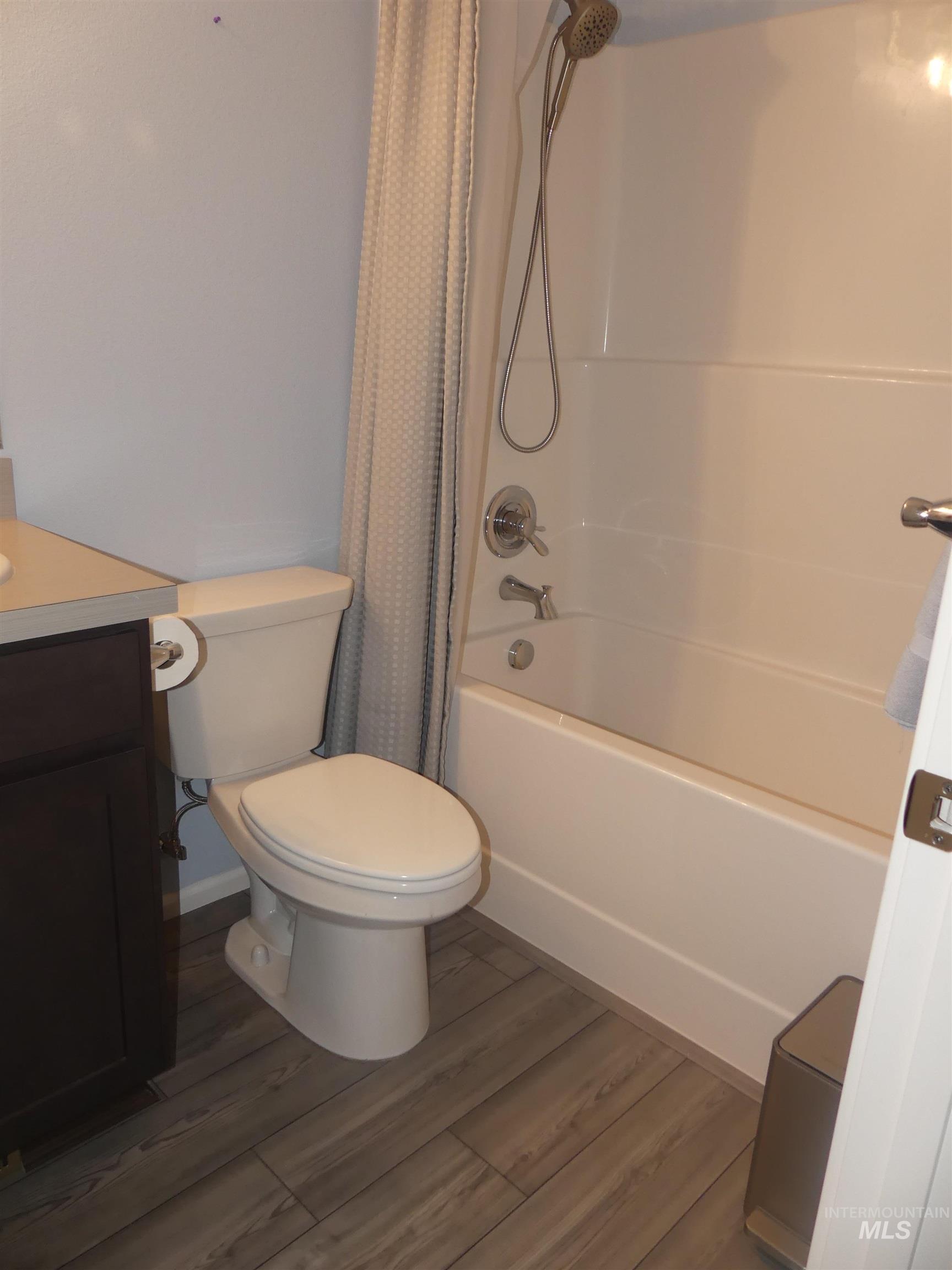 Bathroom featuring shower / bath combo with shower curtain, vanity, and dark wood-style flooring