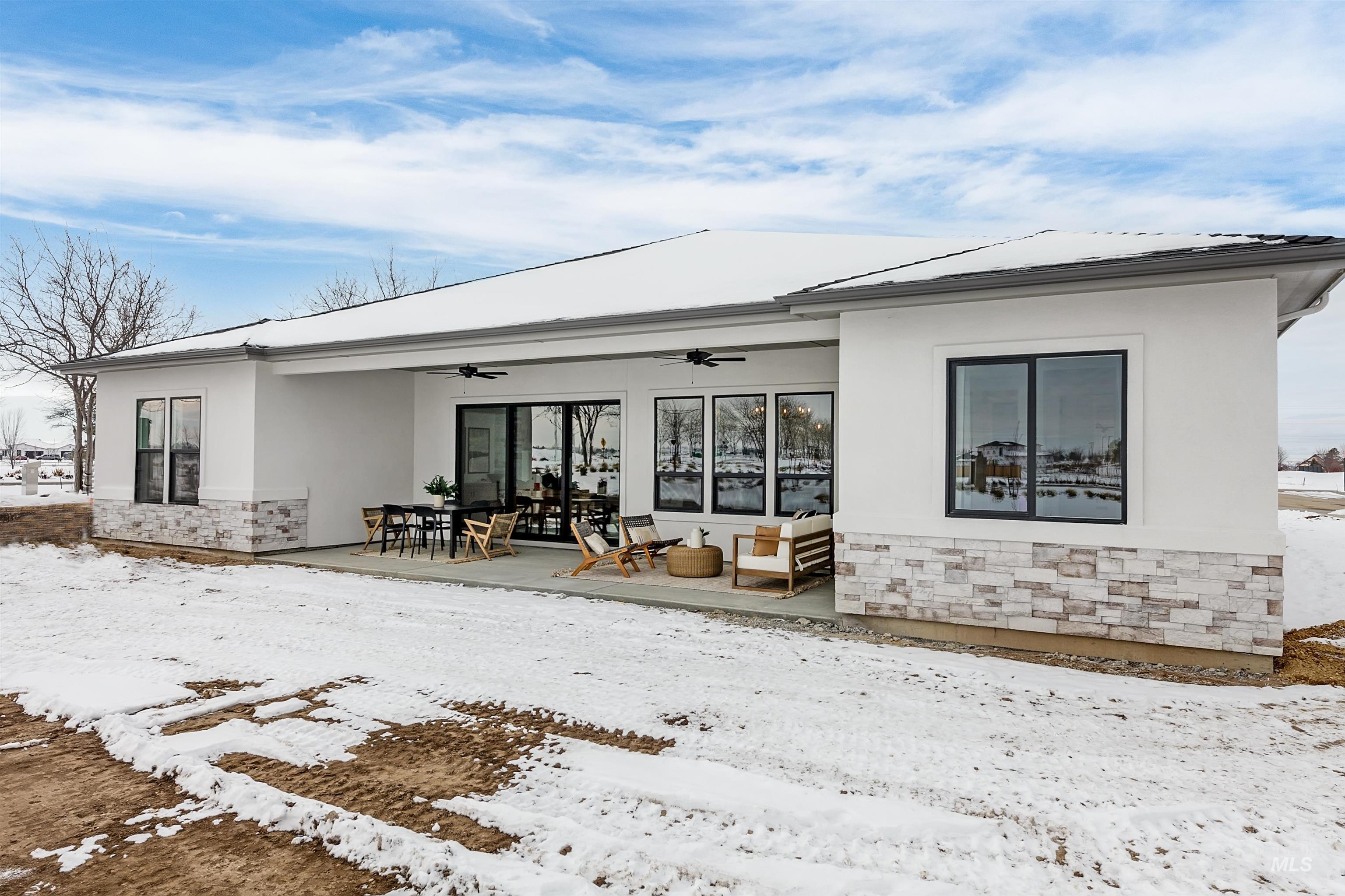 Snow covered rear of property with stone siding, stucco siding, ceiling fan, and a patio