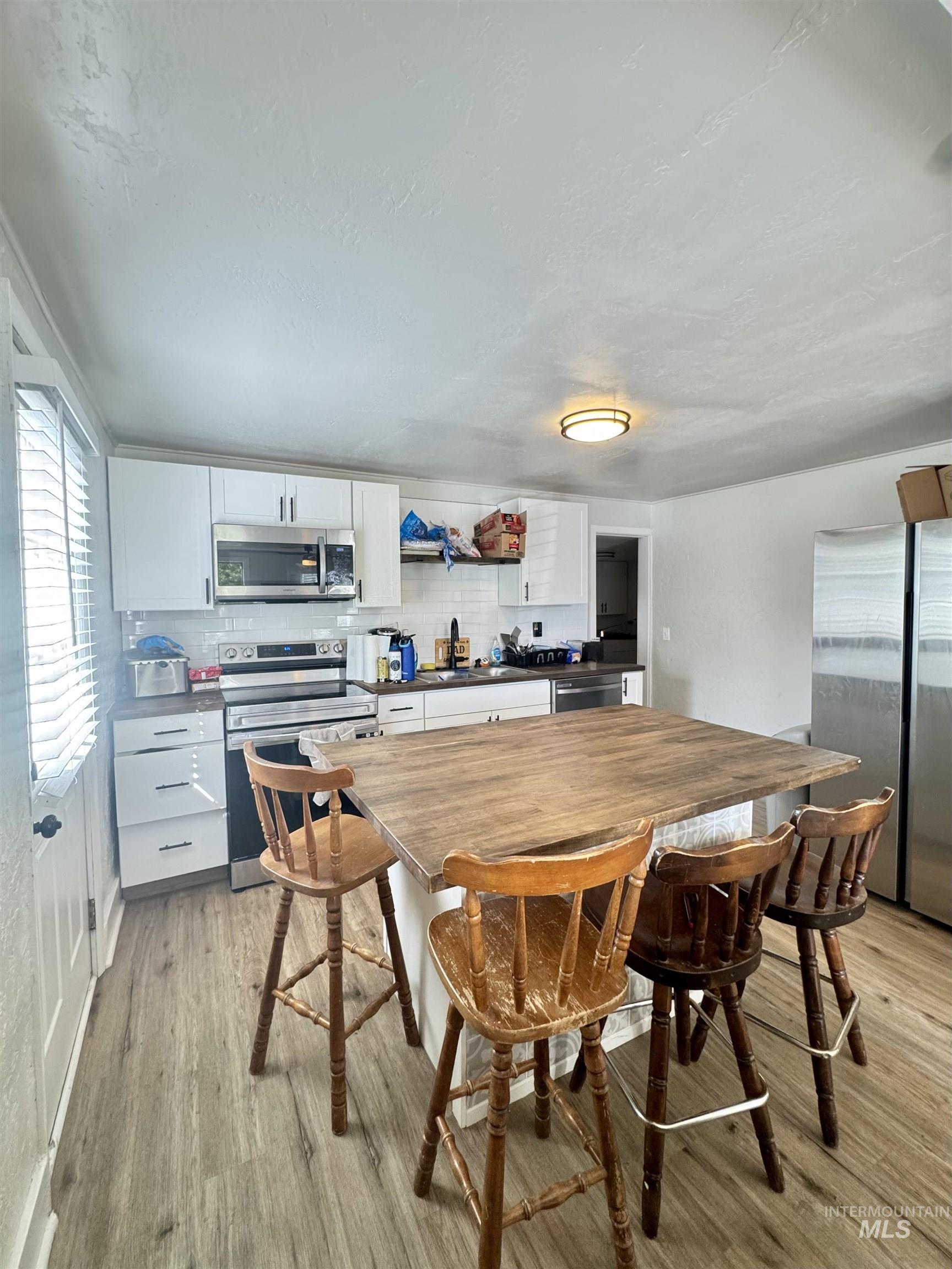 Kitchen featuring white cabinetry, tasteful backsplash, stainless steel appliances, and light wood finished floors