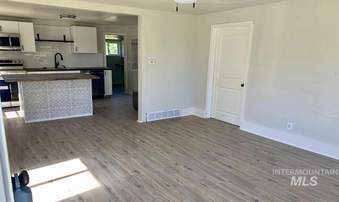 Kitchen with white cabinetry, stainless steel appliances, wood finished floors, tasteful backsplash, and a textured wall