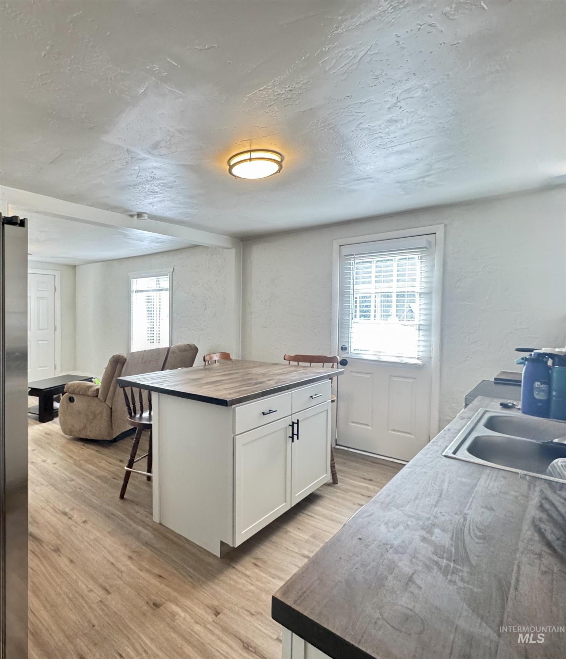 Kitchen featuring wooden counters, a textured ceiling, white cabinetry, light wood-style floors, and a textured wall