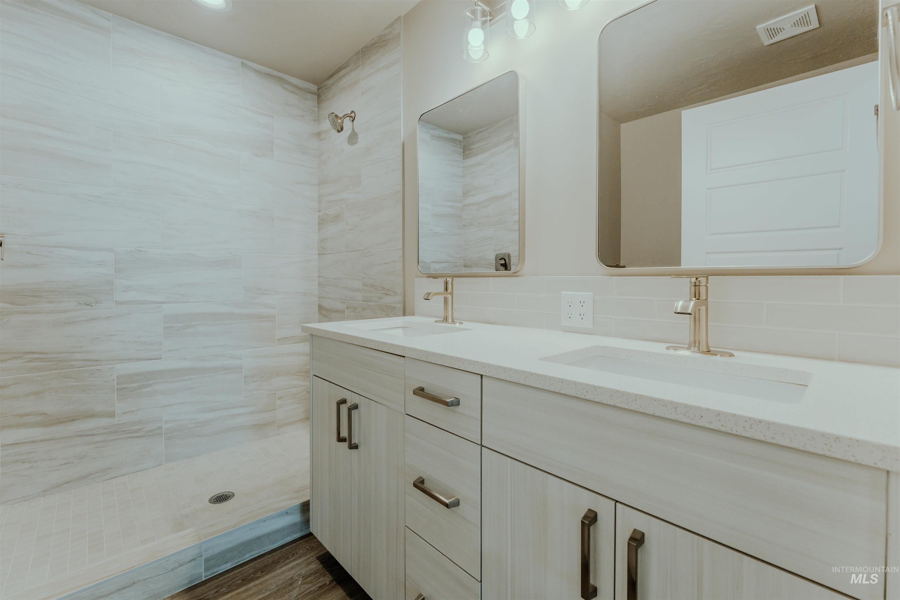 Full bathroom featuring double vanity, a stall shower, backsplash, and dark wood-style floors