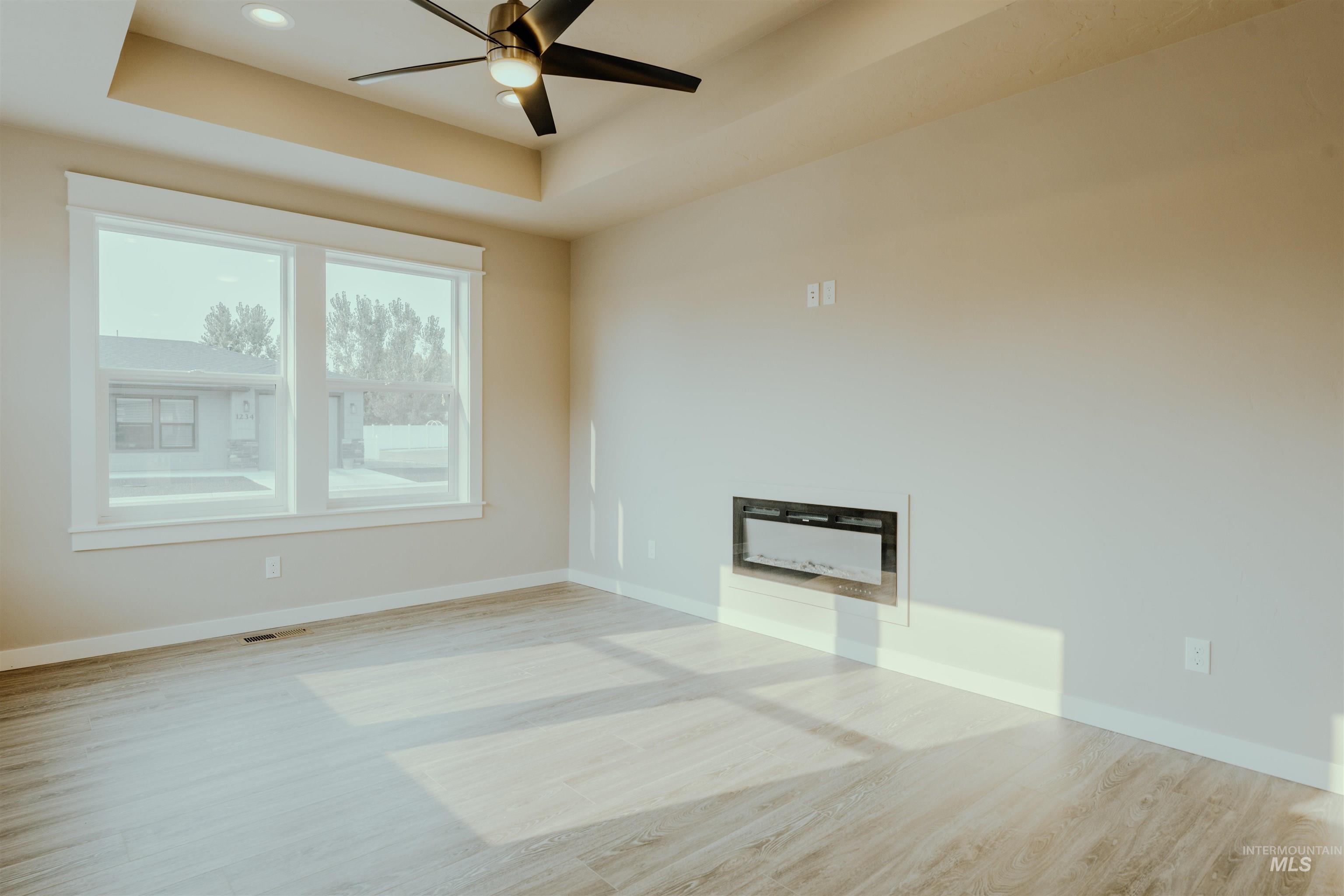 Spare room featuring light wood-style floors, a raised ceiling, and ceiling fan