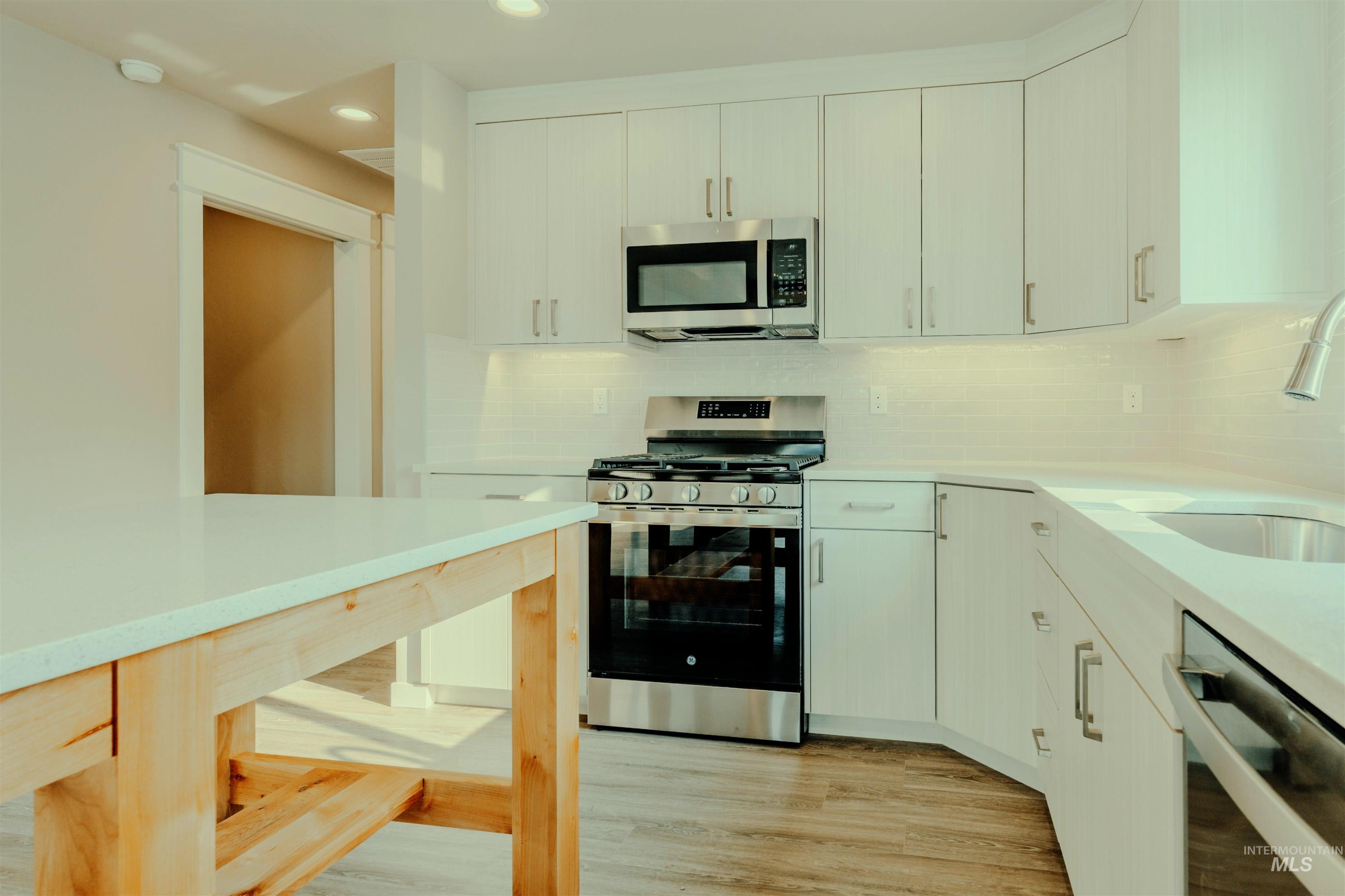 Kitchen with appliances with stainless steel finishes, decorative backsplash, light wood finished floors, light stone counters, and recessed lighting