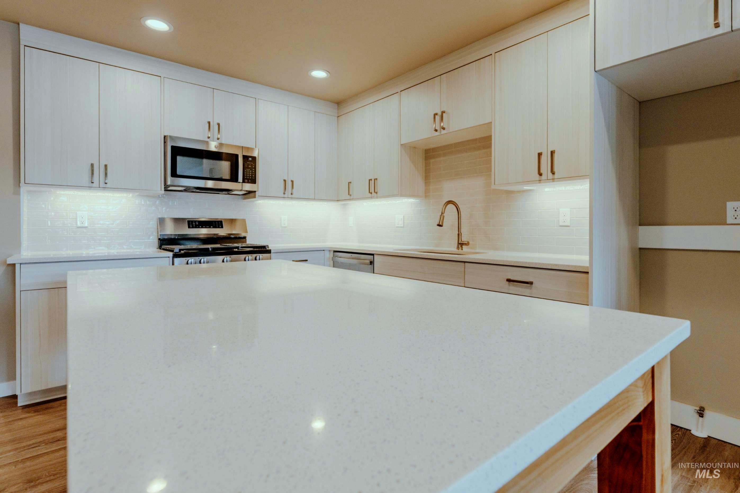 Kitchen featuring light wood-style floors, stainless steel appliances, tasteful backsplash, recessed lighting, and light stone countertops
