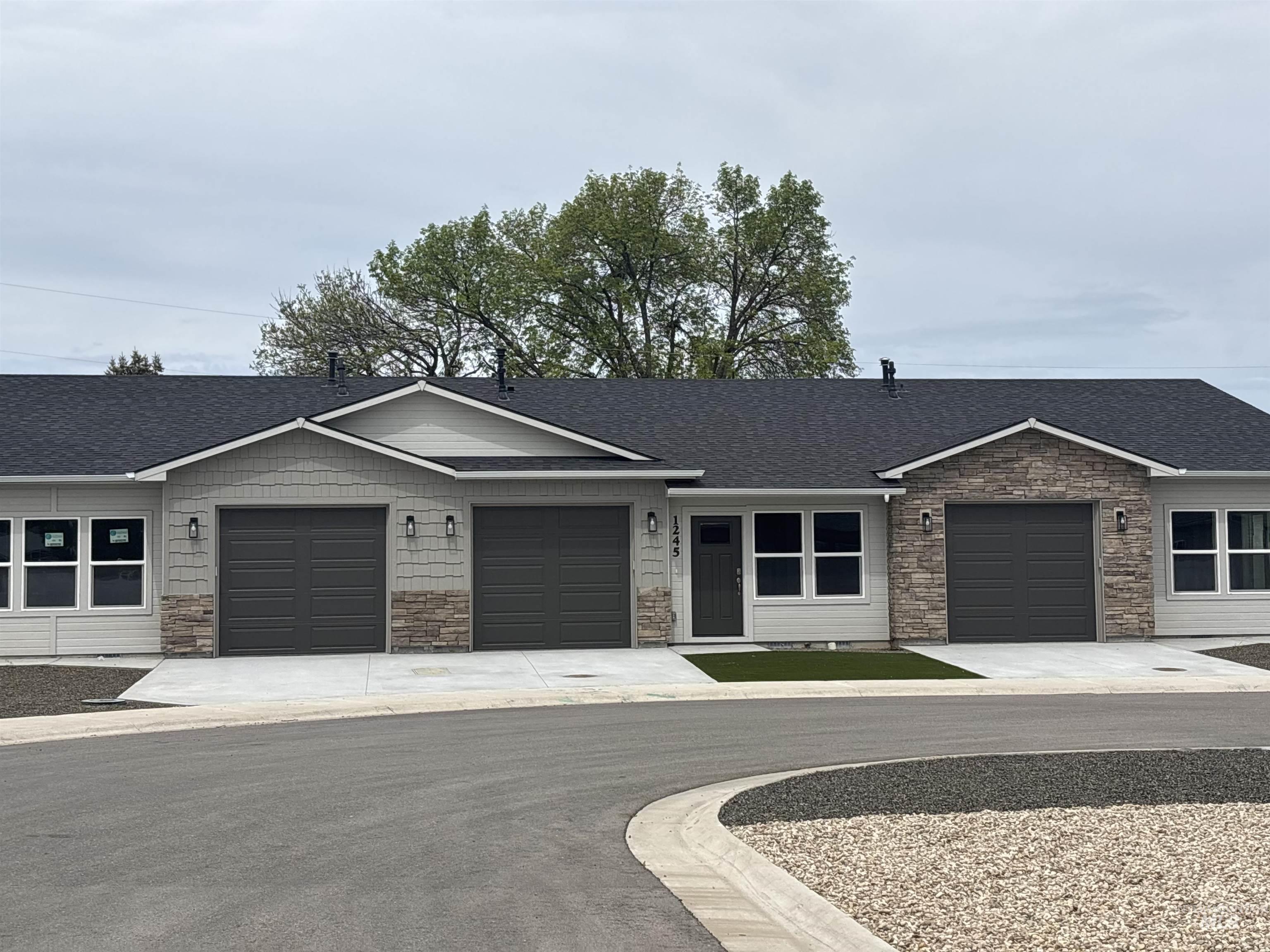Ranch-style home with stone siding, roof with shingles, concrete driveway, and a garage