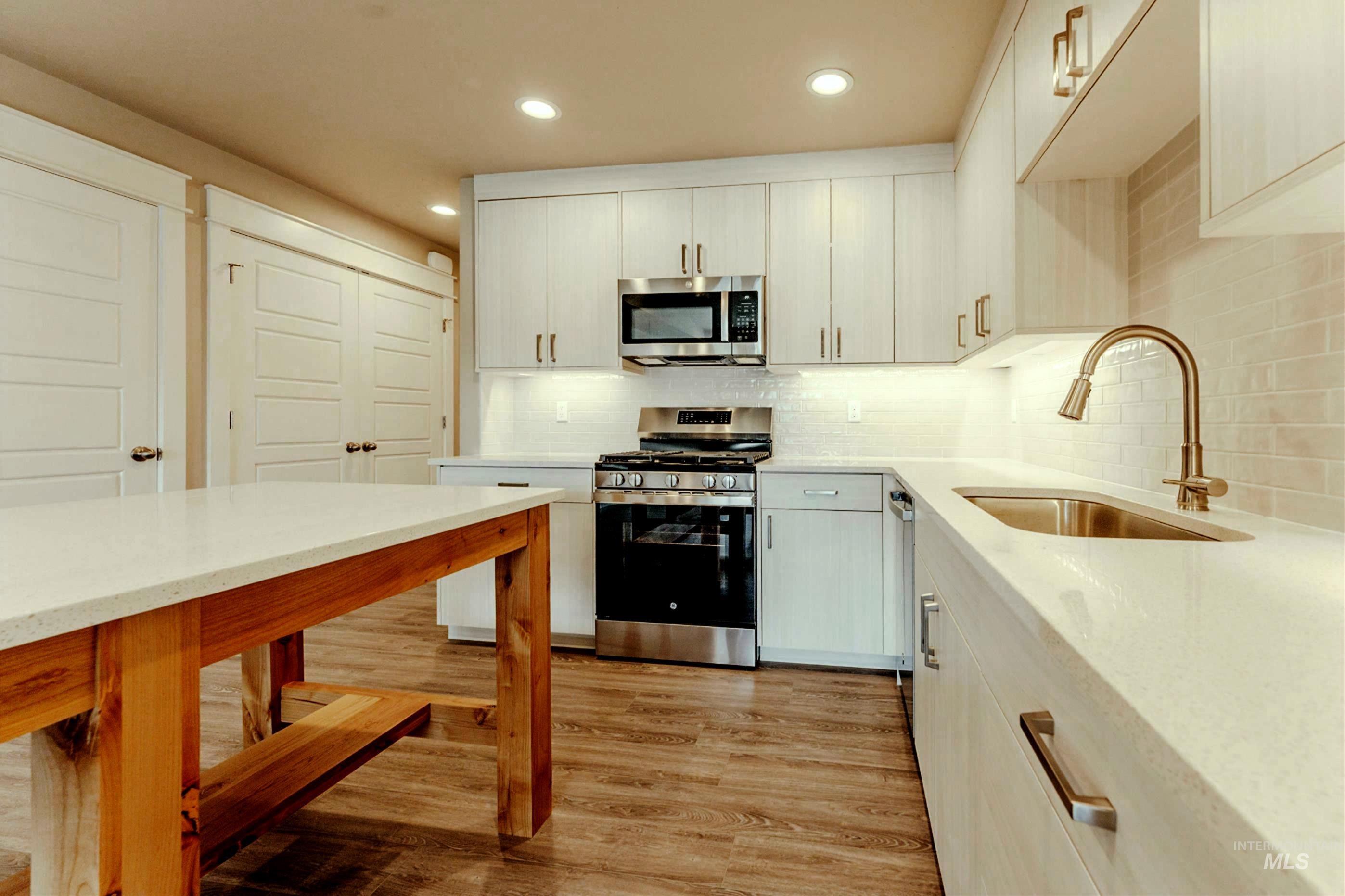 Kitchen with stainless steel appliances, backsplash, light wood-type flooring, light stone counters, and recessed lighting