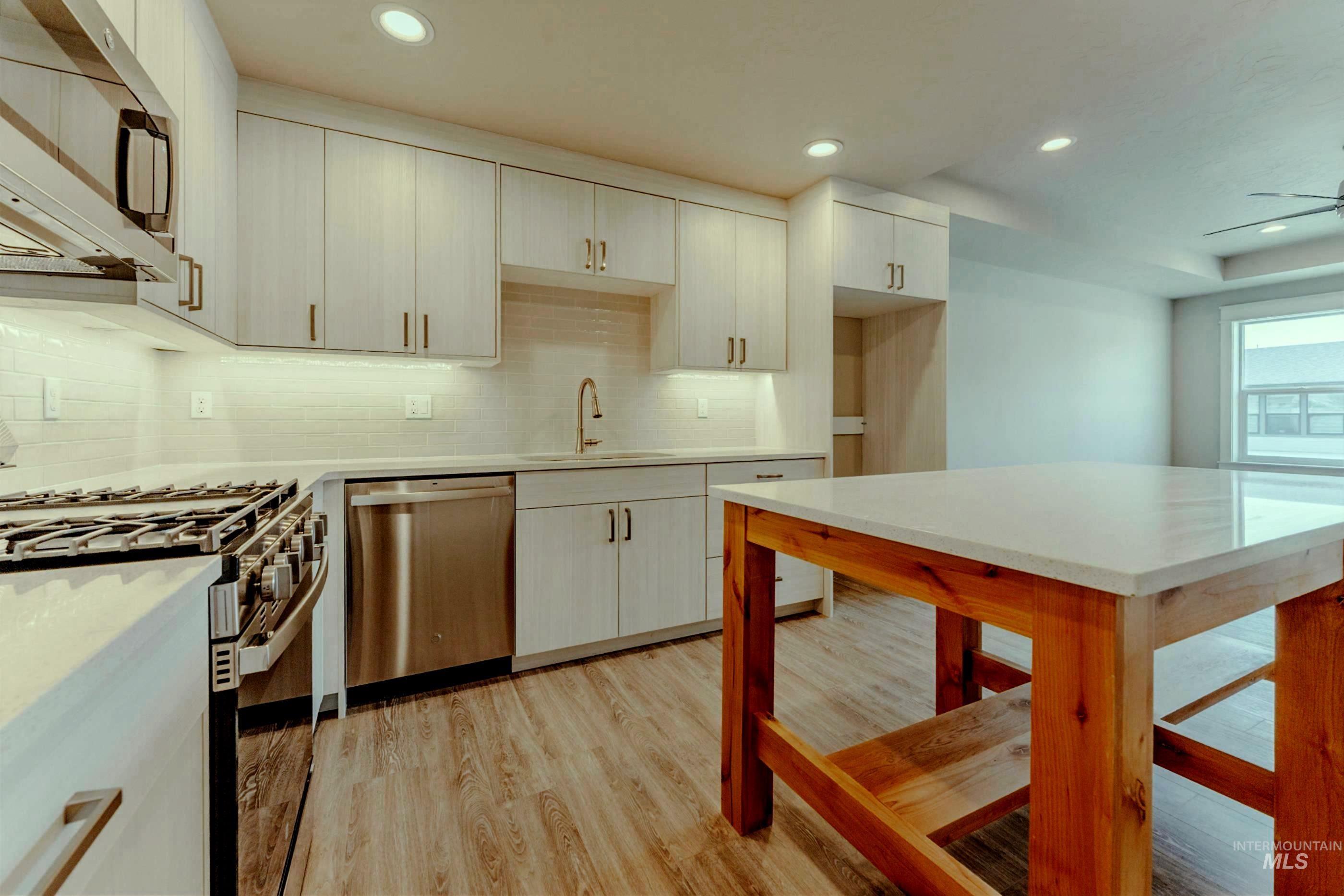 Kitchen featuring stainless steel appliances, light wood-type flooring, backsplash, recessed lighting, and light stone countertops