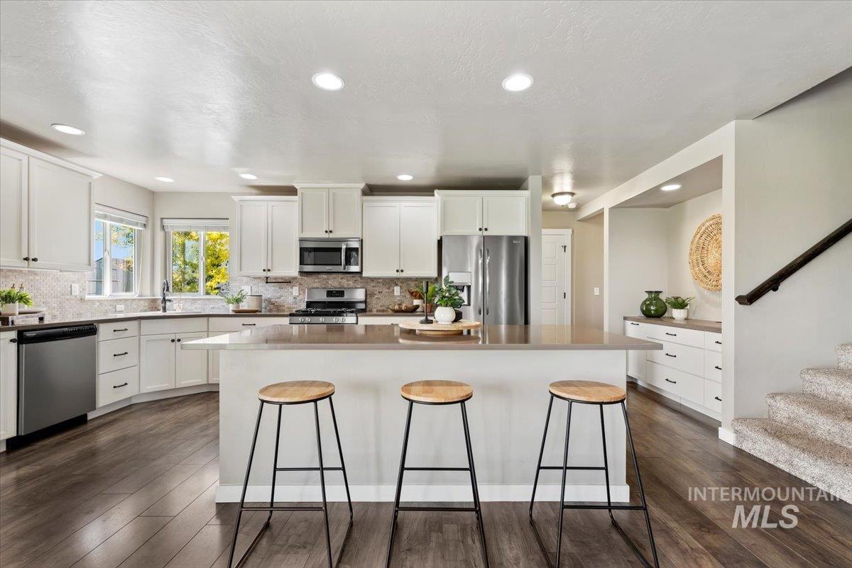 Kitchen with appliances with stainless steel finishes, white cabinetry, a center island, a breakfast bar, and decorative backsplash
