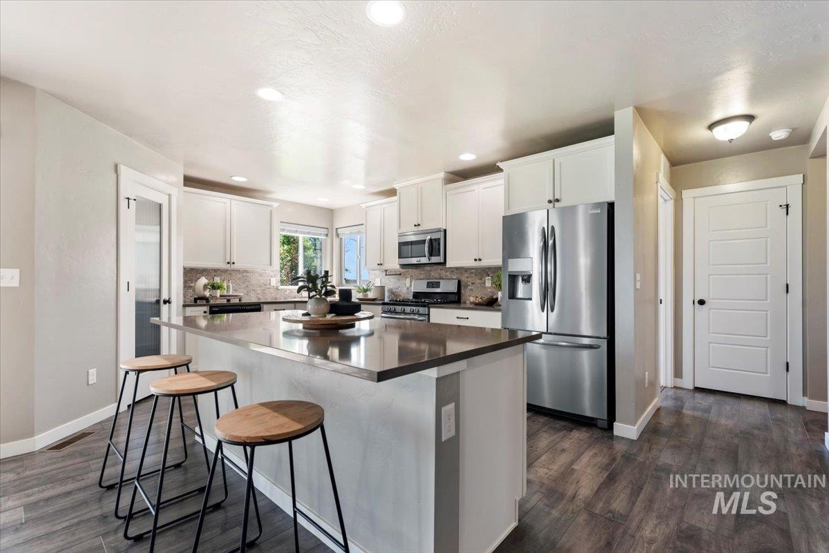 Kitchen with appliances with stainless steel finishes, a breakfast bar area, white cabinets, a kitchen island, and decorative backsplash