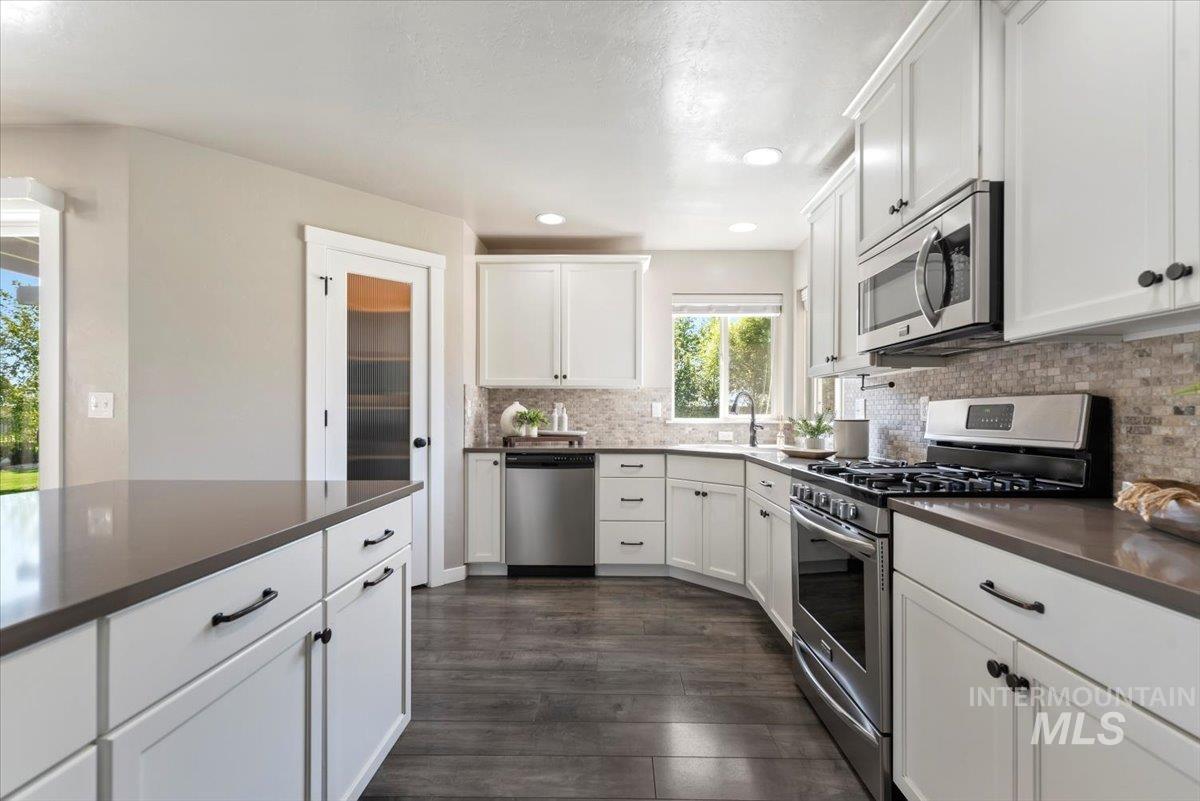 Kitchen featuring stainless steel appliances, white cabinetry, dark wood-style flooring, backsplash, and recessed lighting