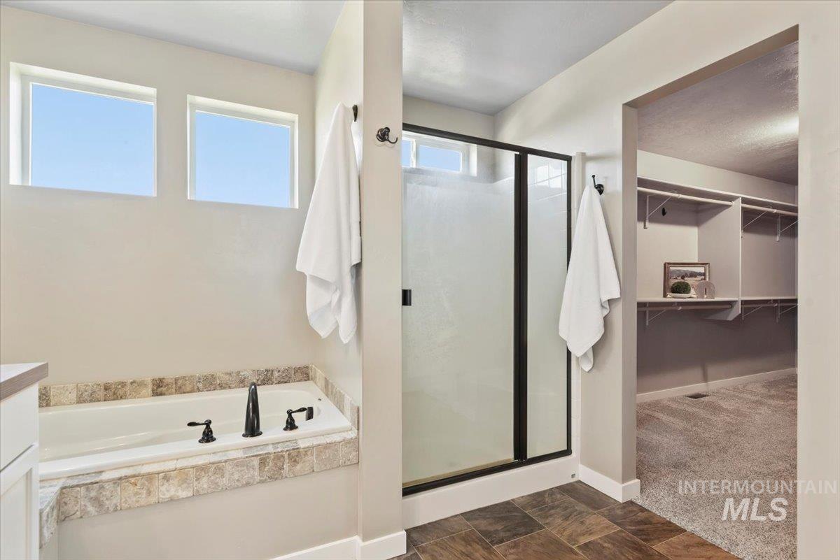 Full bathroom with a shower stall, a bath, a walk in closet, and vanity