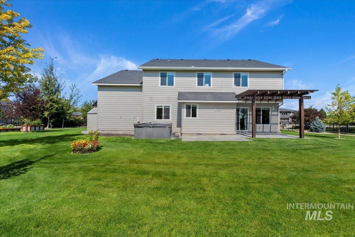 Back of property featuring a hot tub, a patio, a pergola, and a lawn