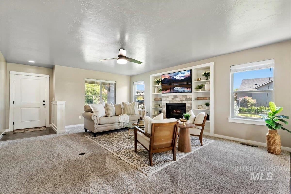 Carpeted living area with a textured ceiling, a ceiling fan, healthy amount of natural light, and a glass covered fireplace